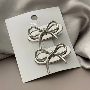 Close-up of polished silver bow hair clips set on card with satin fabric background