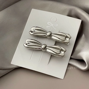 Macro detail of two silver metallic bow hair clips on white card with satin background