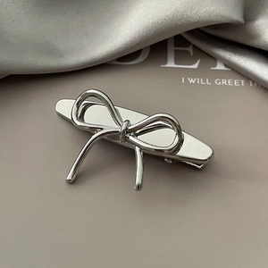 Detail of silver metallic bow hair clip with glossy finish on elegant silk background