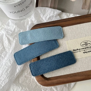 Detailed close-up of three denim fabric rectangular hair clips with neat stitched edges