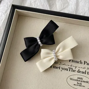 Detail view of pearl bow hair clips in black and cream satin on wooden tray