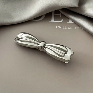 Close-up of a sleek silver metal bow hair clip with a polished mirror finish detail