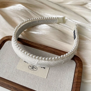 Detailed close-up of cream jacquard headband with pearls on a satin background
