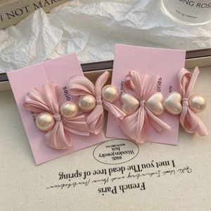 Détail de barrettes à nœud en satin rose avec perles et breloques cœur sur carte rose