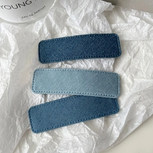 Three pieces of denim fabric rectangular hair clips in varying blue shades with stitching
