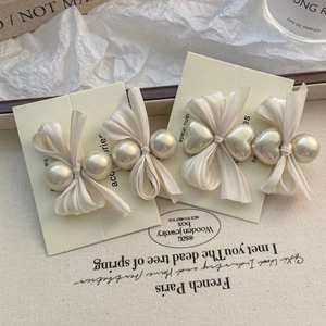 Détail de pinces à cheveux crème avec nœuds en tissu et perles sur fond texturé