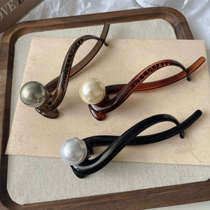 Detailed view of banana-shaped pearl hair clips in dark brown, amber, and black resin