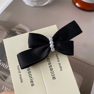 Close-up of black satin bow hair clip with five white pearls on accessory card