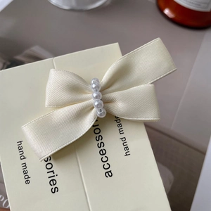 Close-up of cream satin bow hair clip with five white pearls and handmade tag