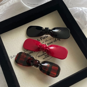 Three elegant bow hair clips in black, red, and plaid pattern on a display board