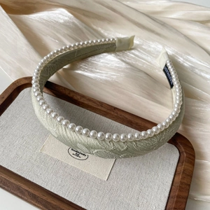 Detail of light green jacquard headband with white pearls on a silk display tray