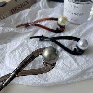 Three elegant twisted hair clips with large pearl accents in amber, black, and smoke grey colors