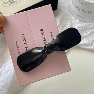 Close-up of black bow hair clip on pink card with stylish perfume bottle background