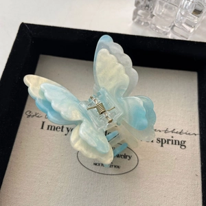 Détail d'une pince à cheveux papillon dégradé bleu et blanc avec paillettes dorées