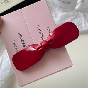 Detail view of a bright red bow-shaped acetate hair clip on a pink display card