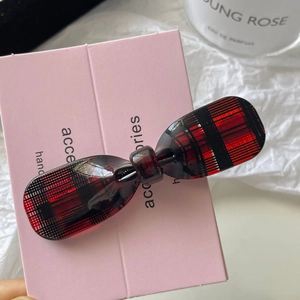 Detail of red checkered acetate bow hair clip on a pink card with a rose perfume background