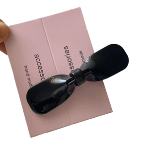 Elegant black acetate bow hair clip on pink display card with glossy finish