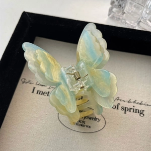 Détail de la pince à cheveux papillon avec texture marbrée bleu-jaune et paillettes