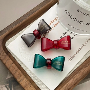 Detailed macro view of acetate bow hair clips in grey, burgundy, and emerald green colors