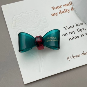 Detail of emerald green acetate bow clip with gold France Handmade logo on art paper