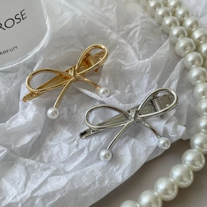 Fermagli per capelli a fiocco in metallo argento e oro con perle su sfondo elegante