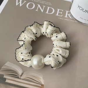 Close-up of cream polka dot scrunchie with lace edges and a large white pearl detail