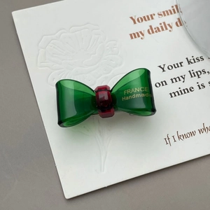 Detailed macro view of green and red translucent acetate bow hair clip with gold lettering