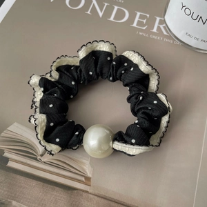 Detail of black polka dot scrunchie with white lace trim and elegant faux pearl