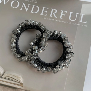 Detail of two silver crystal beaded hair ties on a fashion book with elastic black band