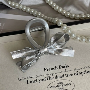 Close-up of matte silver bow hair claw clip with leather texture on display stand