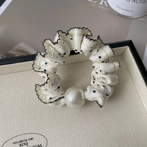 Detail of white polka dot satin scrunchie with large pearl accent on a jewelry tray