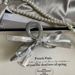 Detail view of a silver leather bow hair claw clip with pearl necklace and satin background