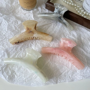 Detail of four large marble pattern hair claws in grey, amber, green and pink colors