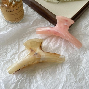 Detailed view of large marble texture hair claws in pink and beige on white background