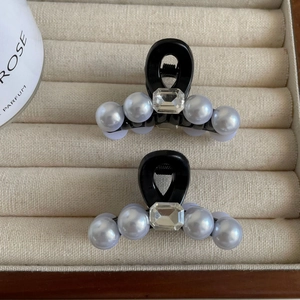 Détail de deux mini pinces à cheveux noires avec perles blanches et cristaux dans un coffret