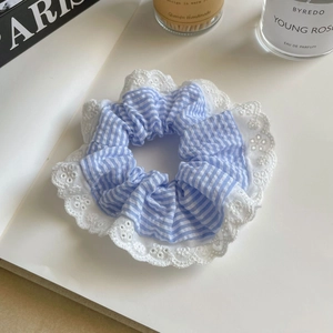 Détail d'un chouchou rayé bleu avec bordure en dentelle blanche sur fond beige neutre