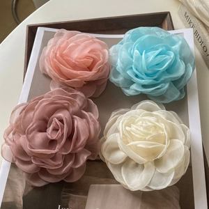 Détail de pinces à cheveux camélia en organza rose et crème sur un plateau en bois