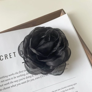 Détail de la pince à cheveux camélia noire faite main sur un plateau avec magazine
