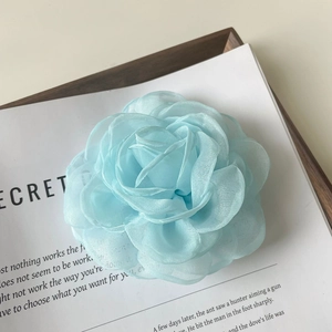 Gros plan d'une pince à cheveux camélia en organza bleu clair sur un plateau en bois
