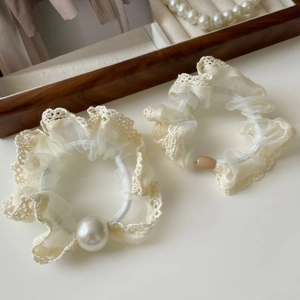 Detail of beige lace hair scrunchies with large imitation pearls on a wooden tray