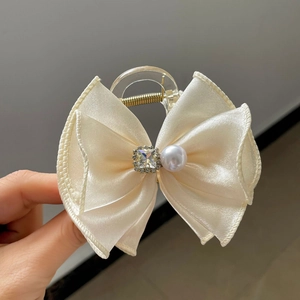 Détail d'une pince à cheveux avec nœud en satin crème, strass brillant et perle