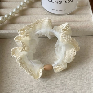 Detail of a creamy lace scrunchie with net mesh edges and a matte brown oval bead