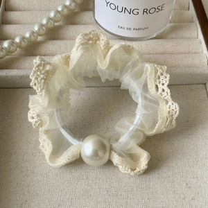 Detail of elegant cream lace scrunchie featuring a large faux pearl on a velvet jewelry tray