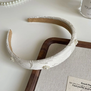 Detail of cream padded headband with floral embroidery and pearl ornaments on white background
