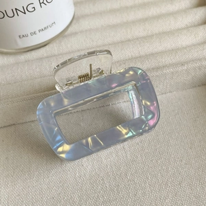 Gros plan d'une pince à cheveux carrée holographique aux reflets irisés sur tissu