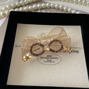 Détail de la pince à cheveux avec nœud en maille doré champagne et strass dans un coffret cadeau