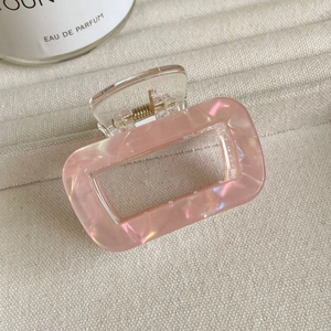Détail de la pince à cheveux en acétate rose nacré avec ressort doré sur tissu tressé