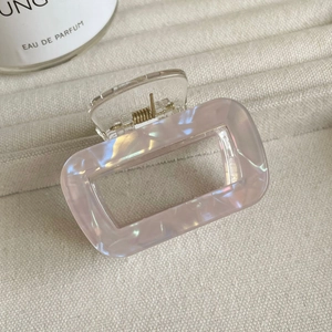 Gros plan sur une pince à cheveux rectangulaire creuse nacrée sur un tissu beige