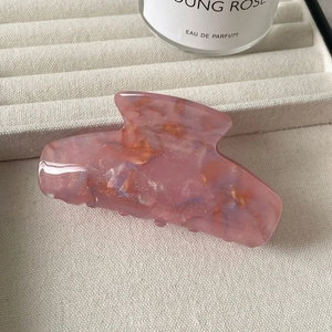Nahaufnahme einer Haarklammer aus rosa Marmor-Acetat mit Goldglitzer auf beigem Tablett