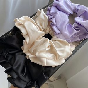 Lot de trois chouchous en satin noir, crème et lilas présentés sur un plateau gris